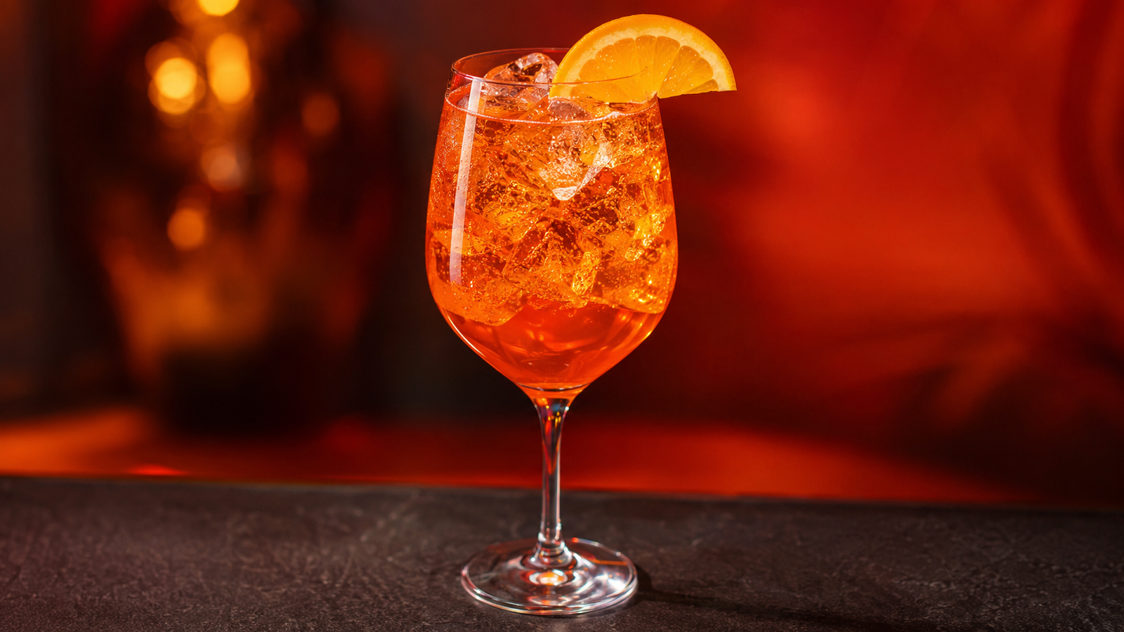 Alkoholfreier Aperol Spritz vor extrem unscharfem Neonhintergrund in der Farbe des Drinks