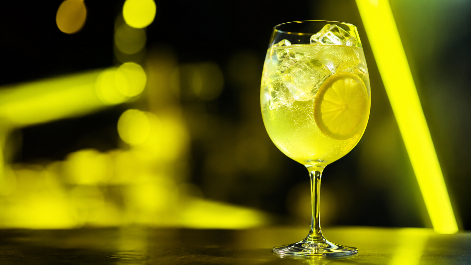 Limoncello Spritz vor extrem unscharfem Neonhintergrund in der Farbe des Drinks